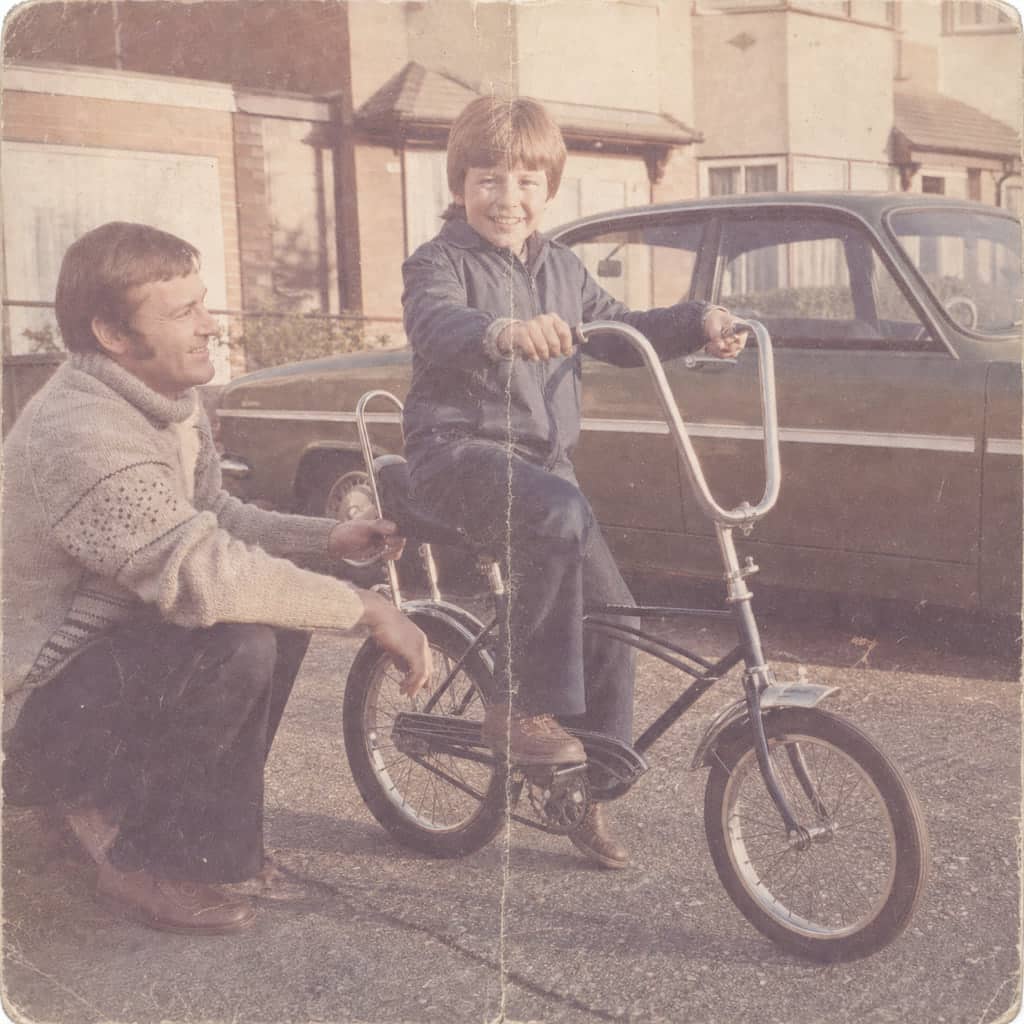 Almost fully faded 1972 print of a boy on a new bicycle with his father, kept exactly as scanned.