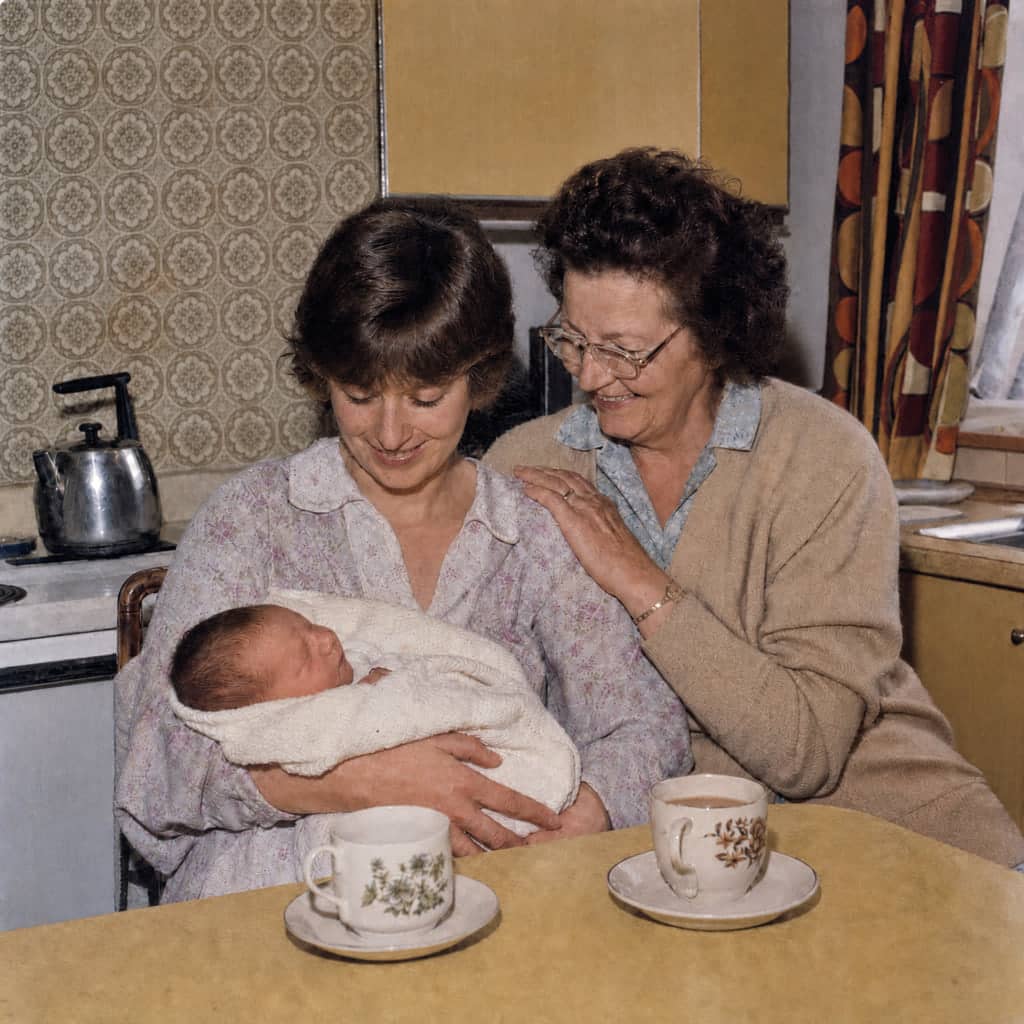 The same kitchen photo after restoration: creases repaired, natural colour, the two women and the baby unchanged.